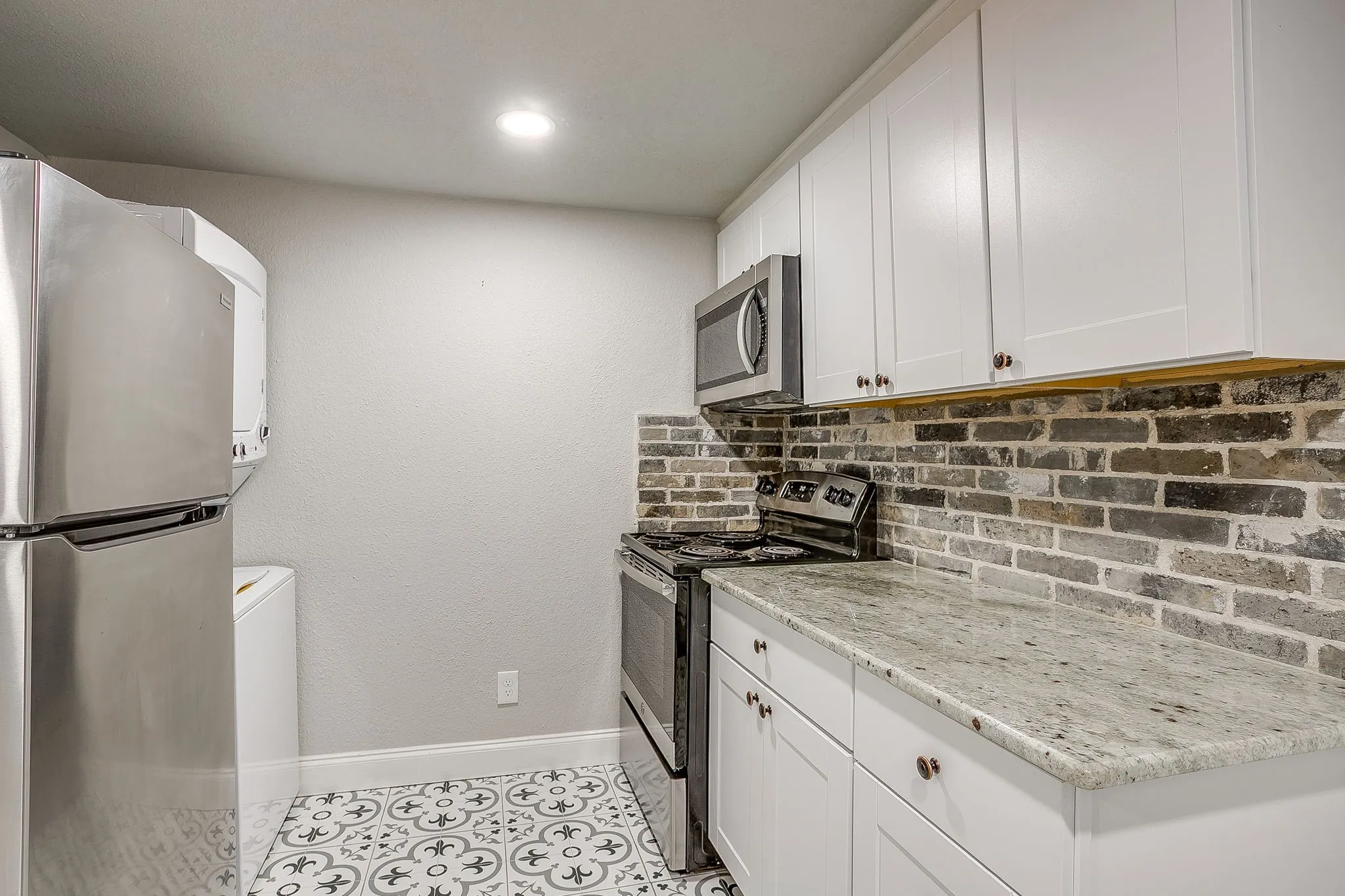 Kitchen featuring stainless steel appliances, white cabinetry, a stone-finish countertop, and decorative tile flooring