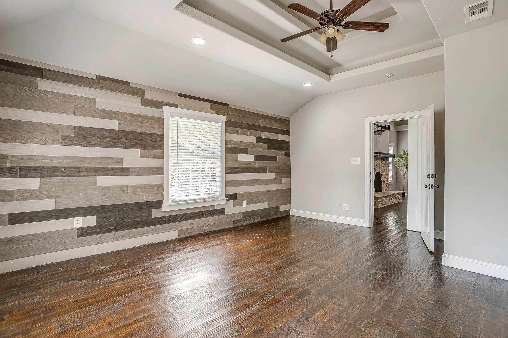 Tray ceiling with a ceiling fan, recessed lighting, wood-finish flooring, and a decorative paneled accent wall