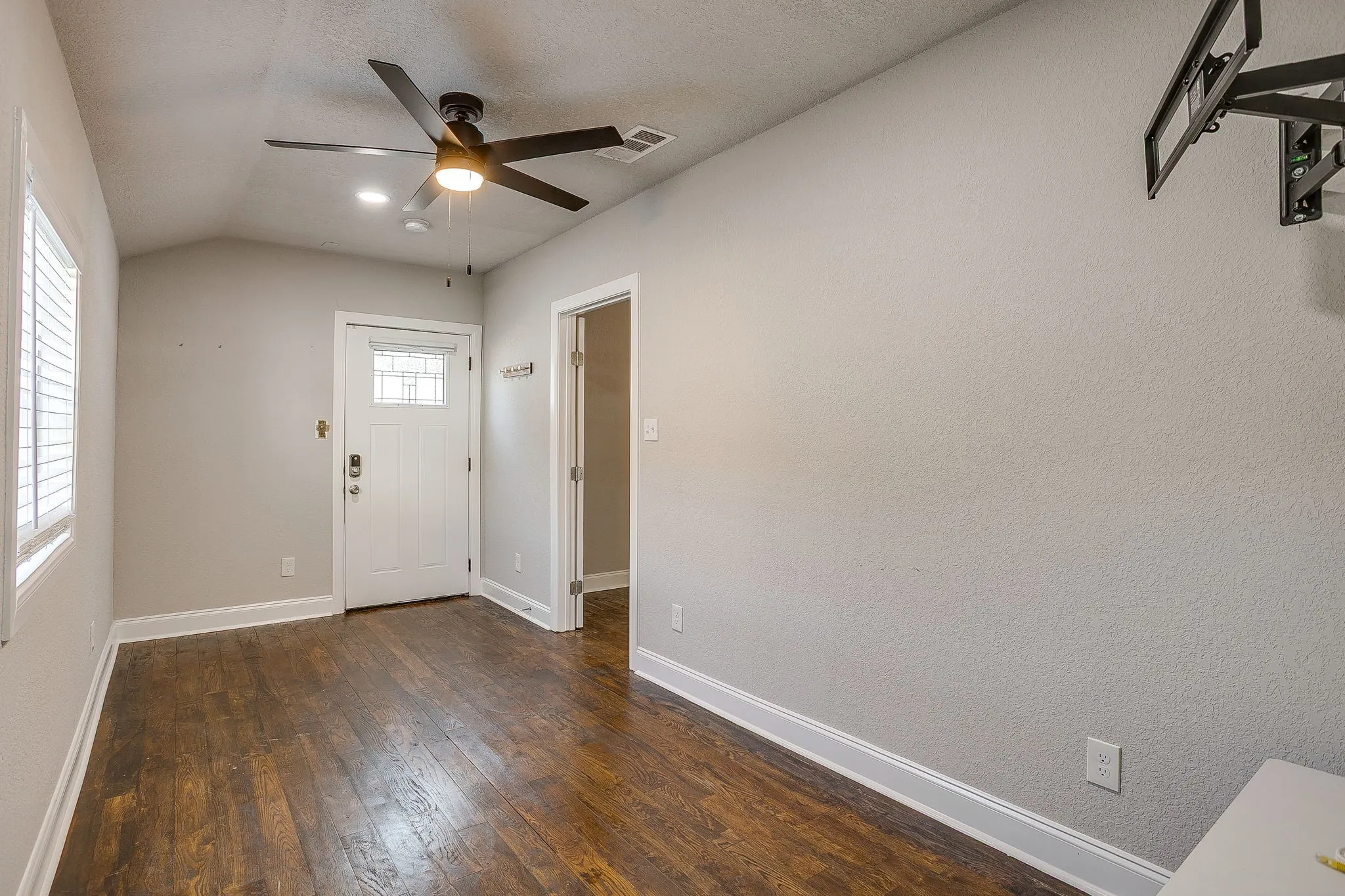 Wood-finish flooring, white trim, ceiling fan with integrated lighting, and a white door with decorative glass inlay