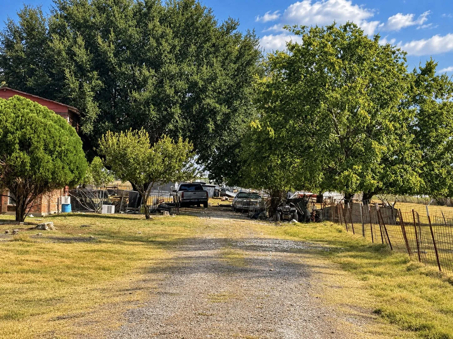 Gravel driveway with mature trees and a brick exterior