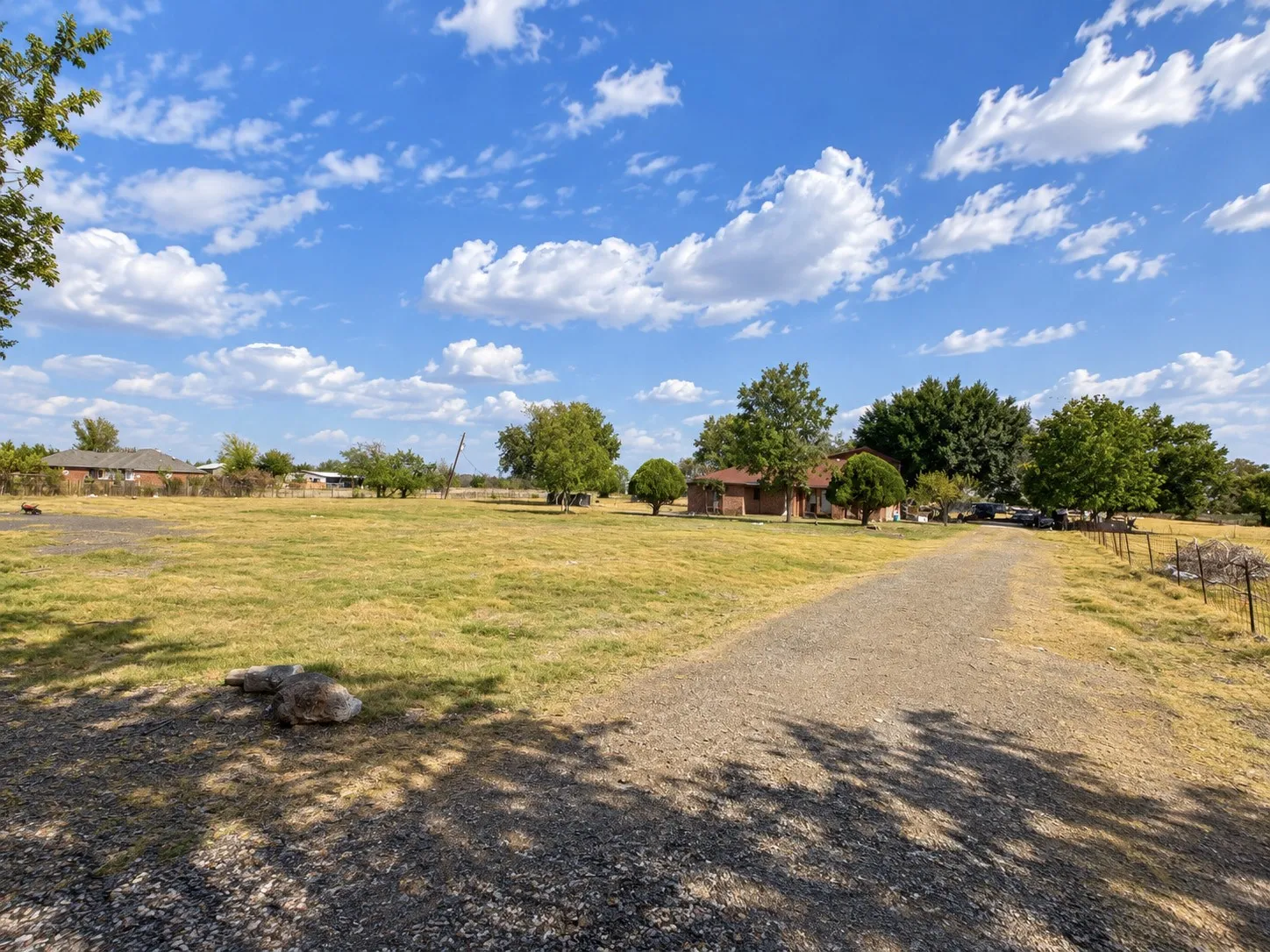 Expansive outdoor grounds featuring a gravel drive, mature trees, and a wire fence