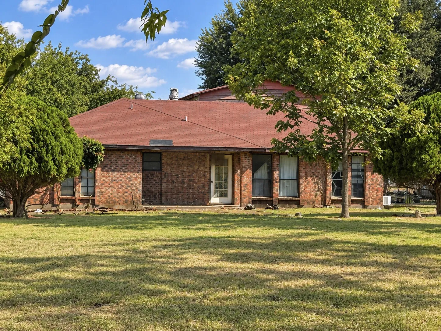 Brick exterior with multiple windows, a red shingle roof, and established landscaping