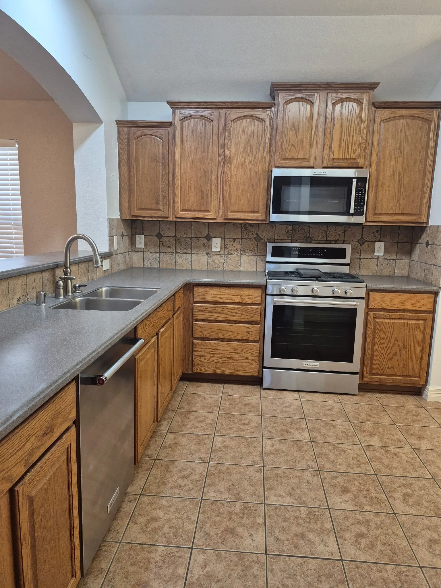 Kitchen featuring wood cabinetry, stainless steel appliances, a double basin sink, tile flooring, and a decorative tile backsplash