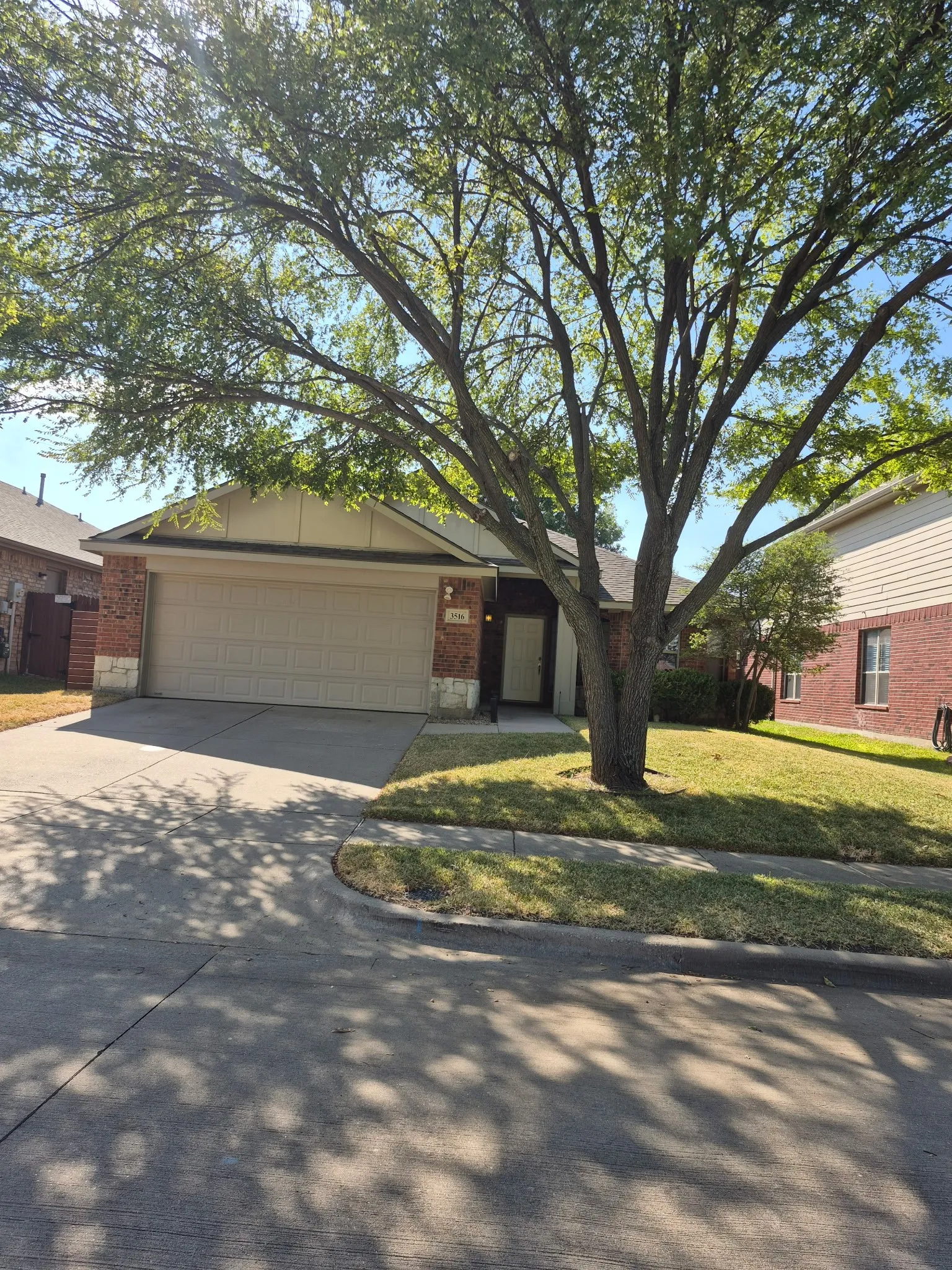 Brick and stone-clad exterior with an attached garage, paved driveway, and established front yard landscaping