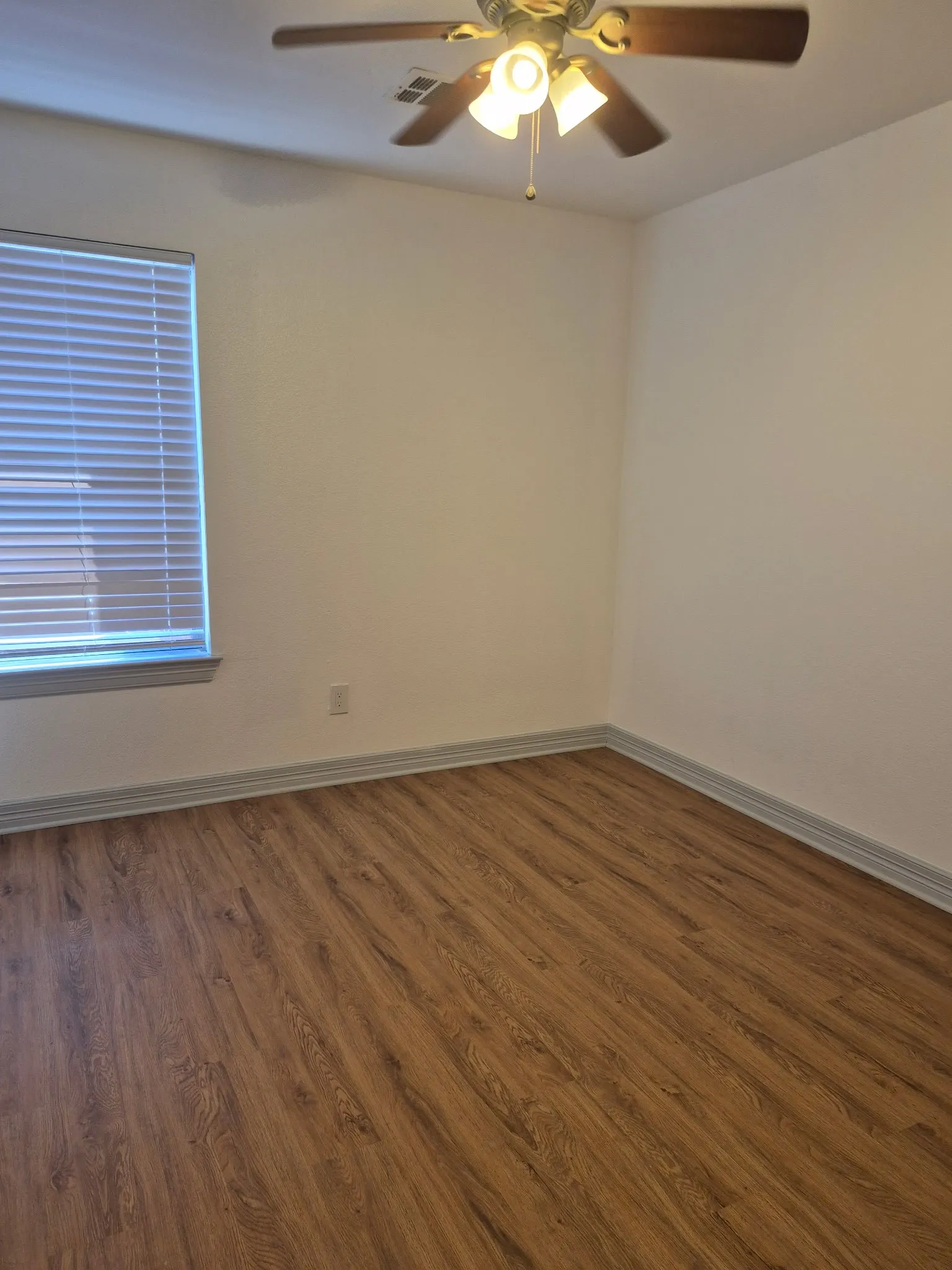 Wood-finish flooring, ceiling fan with integrated lighting, and window with blinds