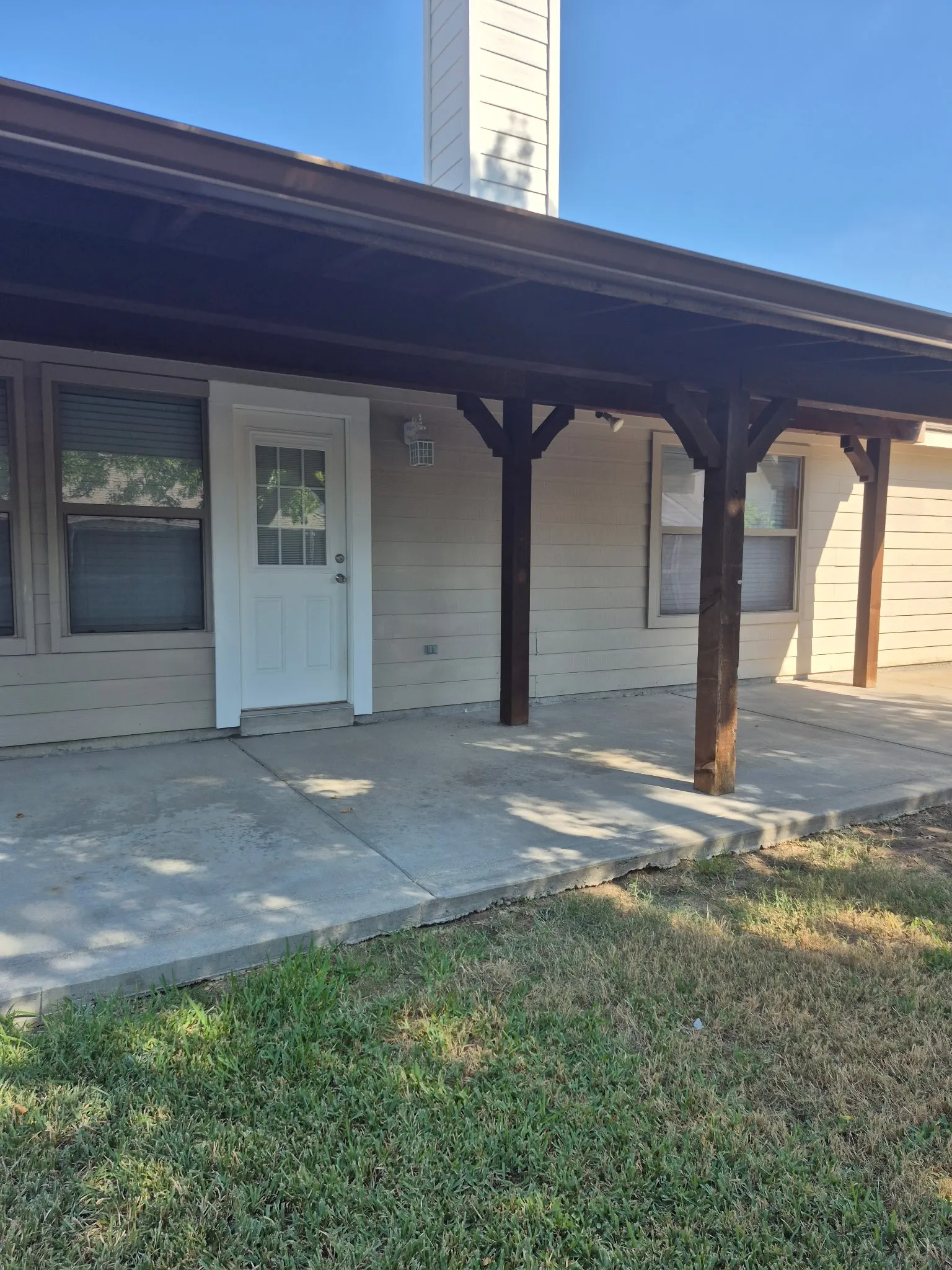 Covered patio with exposed wood beams, concrete slab, and light-colored siding