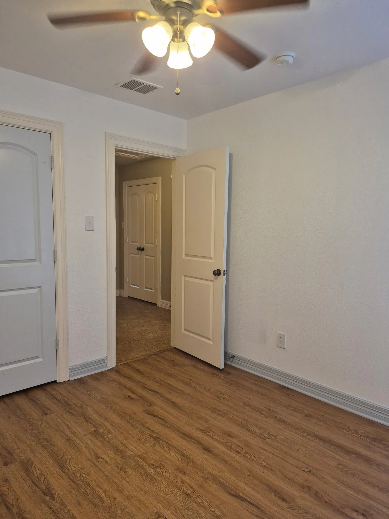 Wood-finish flooring, white painted walls, and ceiling fan with integrated lighting