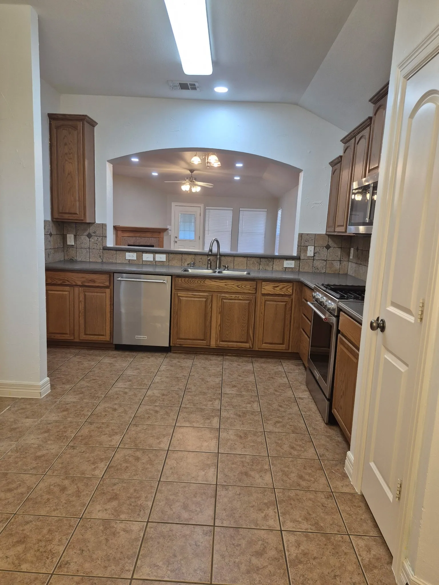 Kitchen featuring wood cabinetry, stainless steel appliances, tiled flooring, dark countertops, and a tiled backsplash