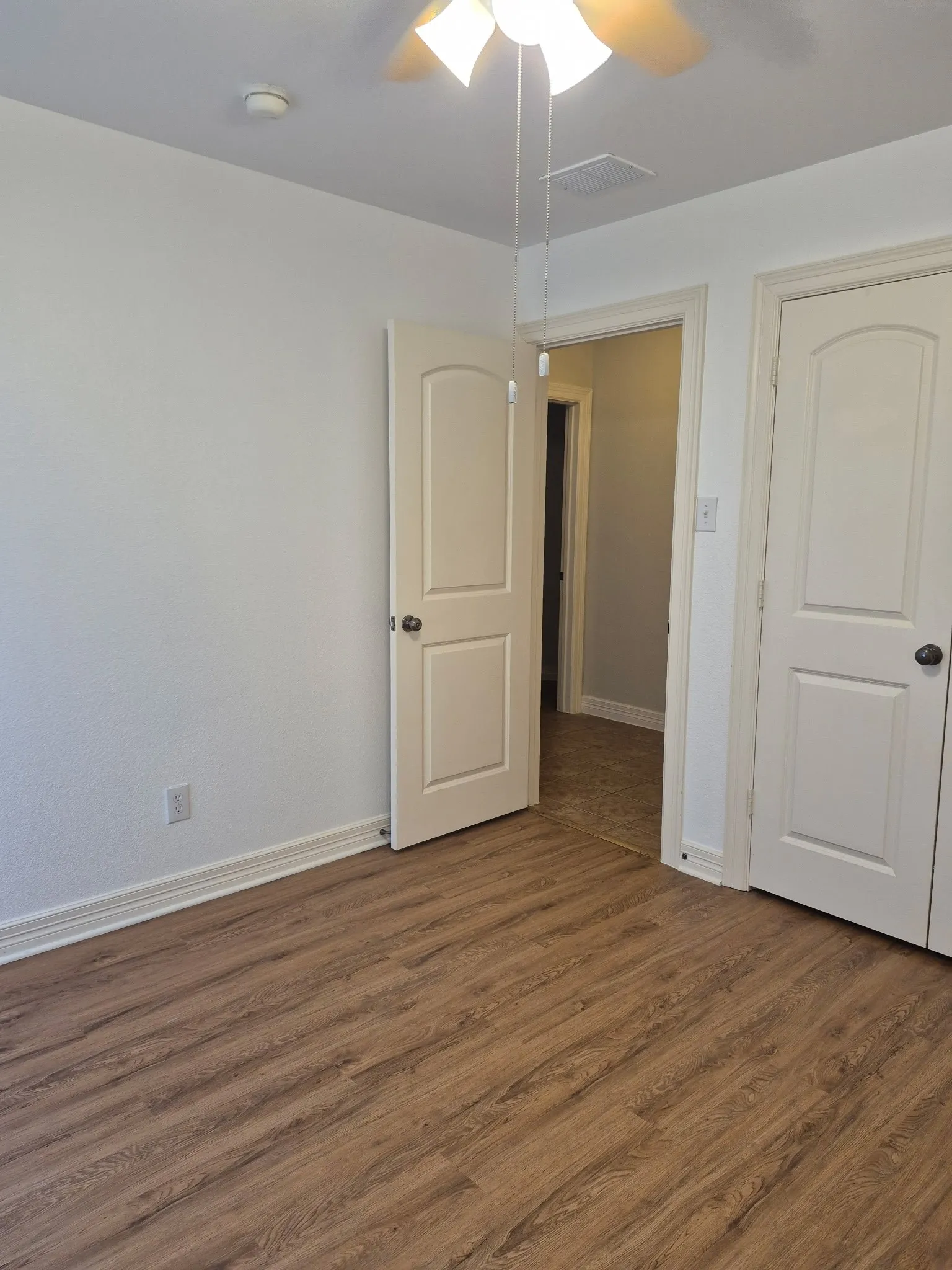 Wood-finish flooring throughout, white painted walls, white trim, and a ceiling fan with integrated lighting