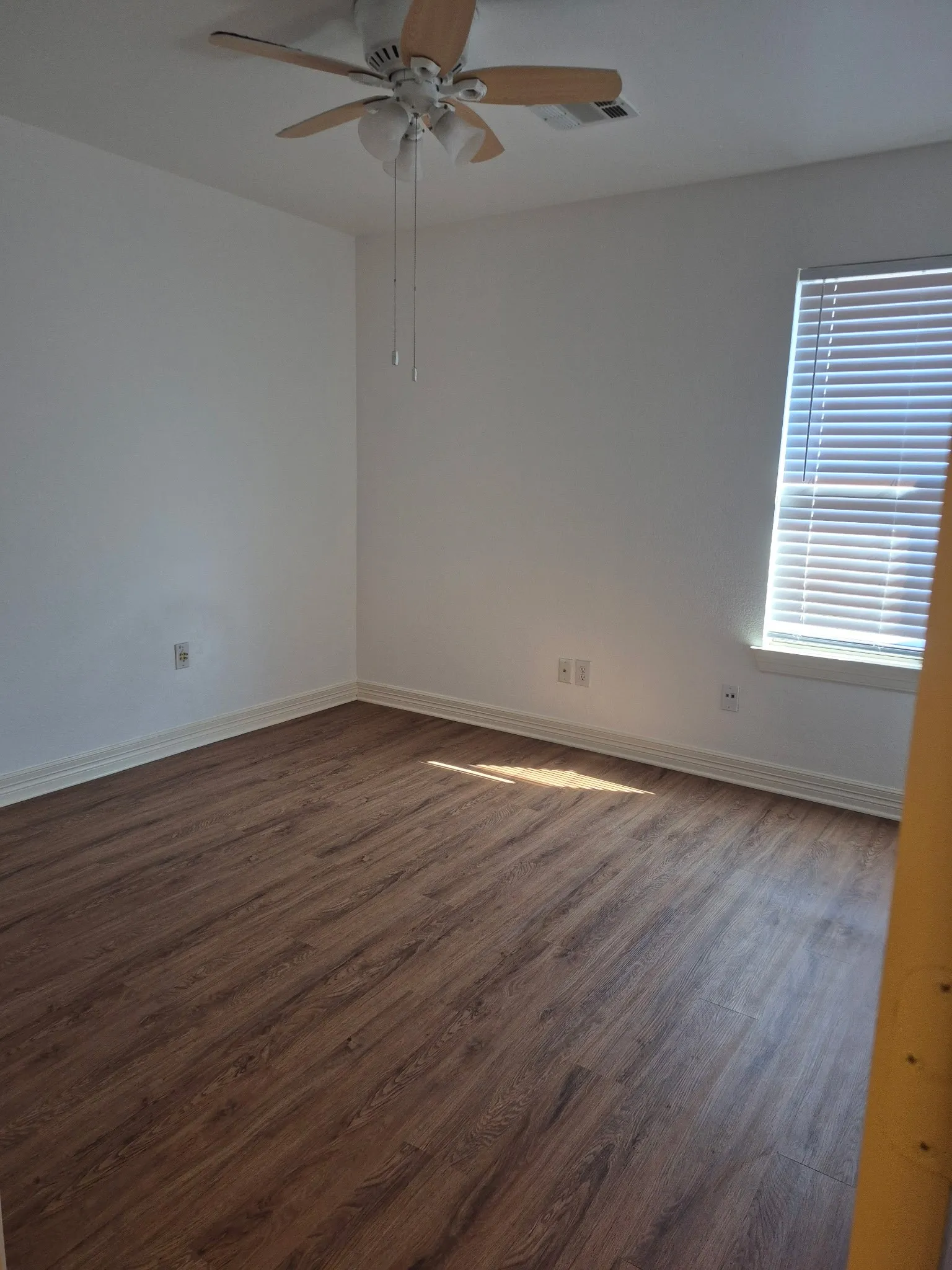 Wood-finish flooring, white walls, ceiling fan, and a window with blinds