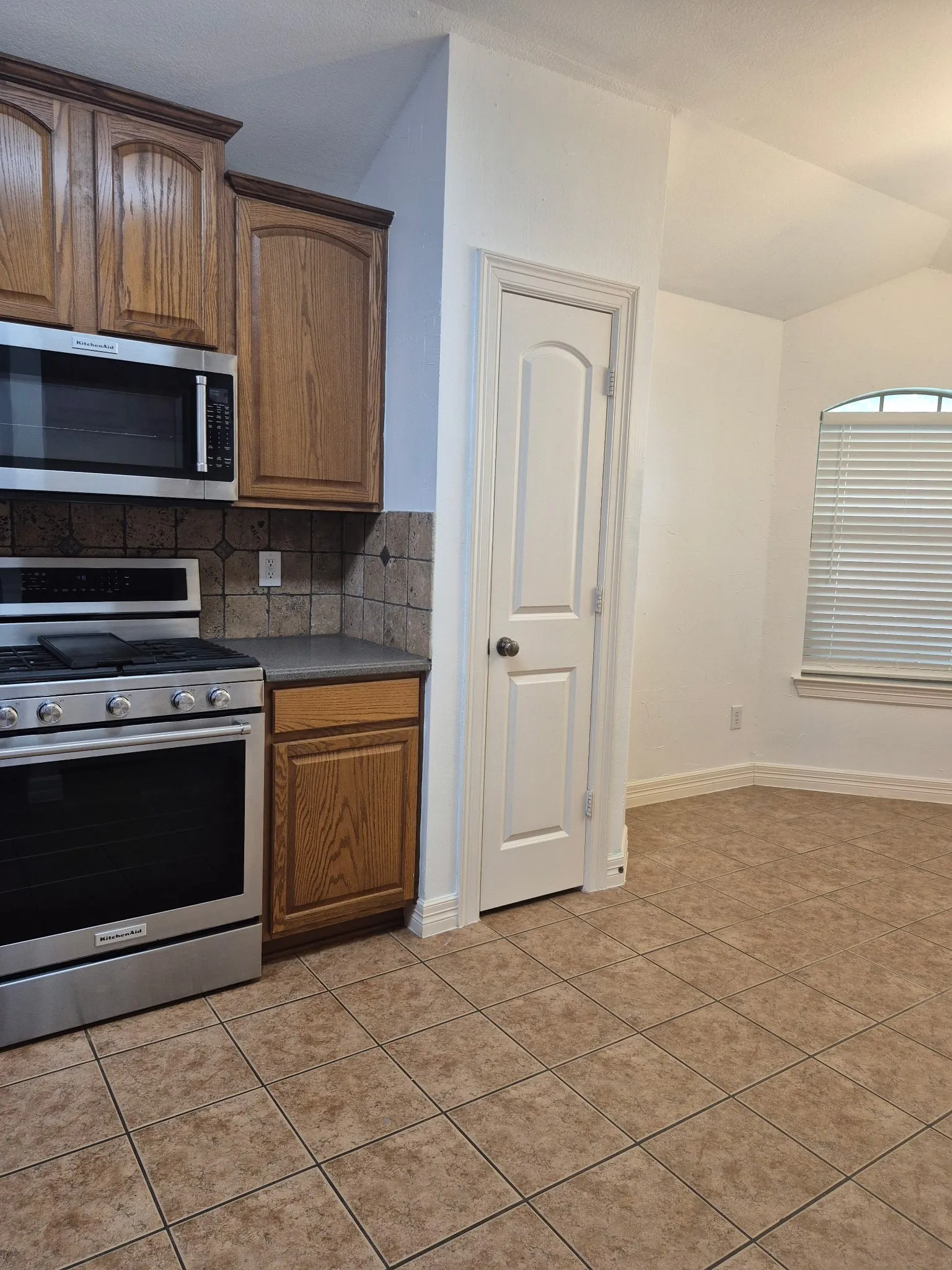 Kitchen featuring stainless steel appliances, wood cabinetry, tile backsplash, and tile flooring
