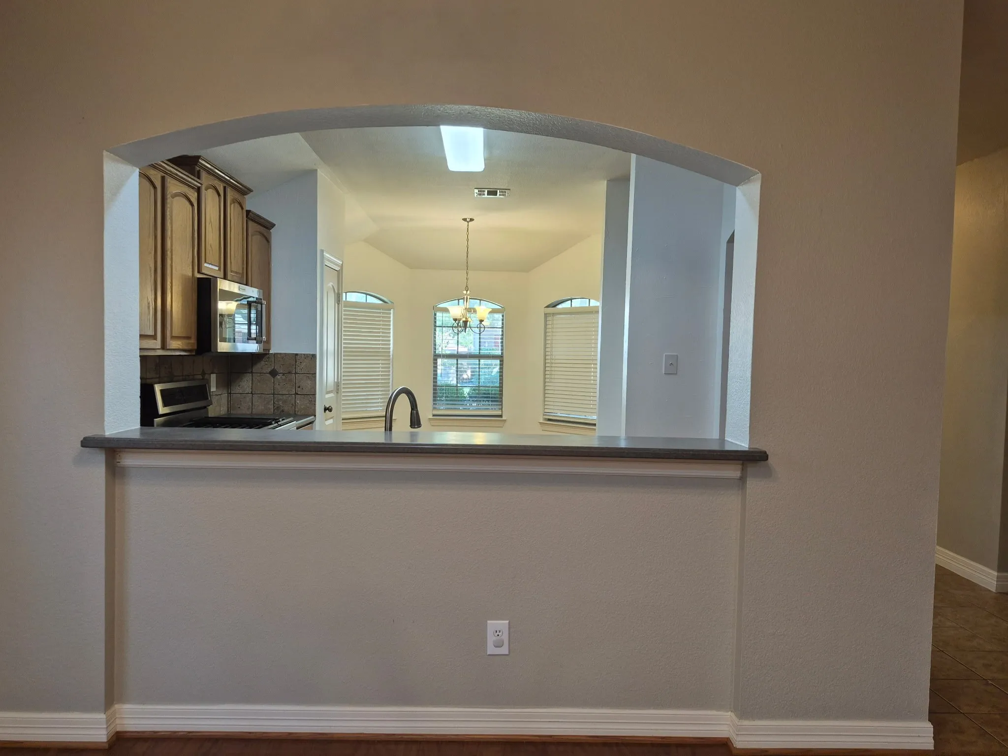 Open arched pass-through with a breakfast bar, wood-finish flooring, and a kitchen featuring wood cabinetry and a tile backsplash