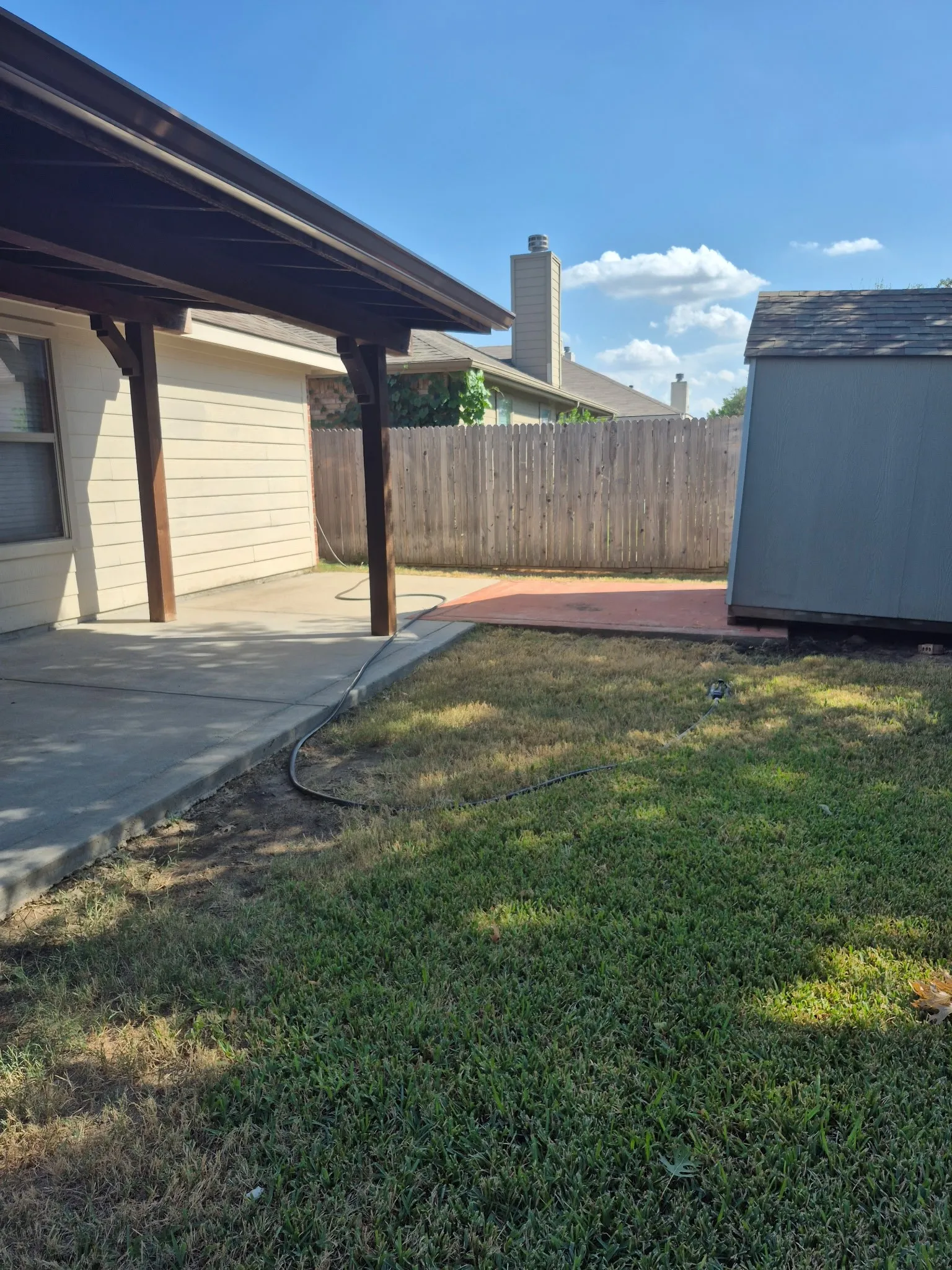 Covered patio with a concrete surface, adjacent to a grassy lawn