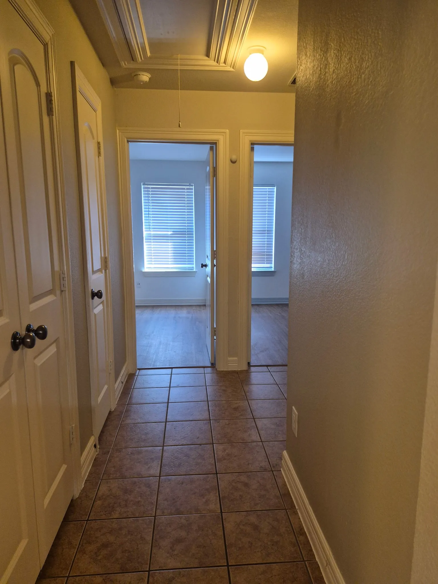 Hallway featuring tile flooring, multiple storage closets, and decorative ceiling trim