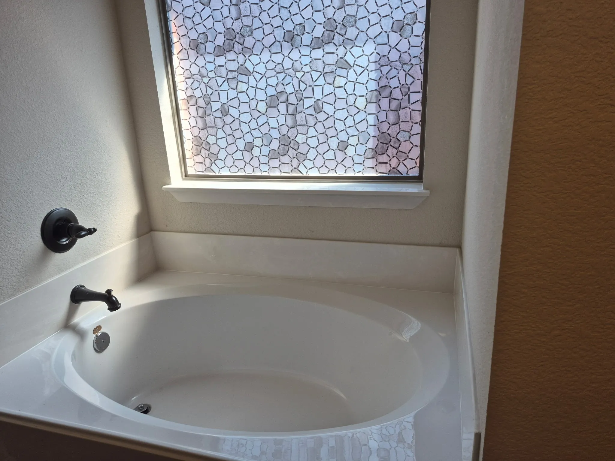 Built-in soaking tub with dark-bronze fixtures, white surround, and a privacy window featuring a geometric pattern