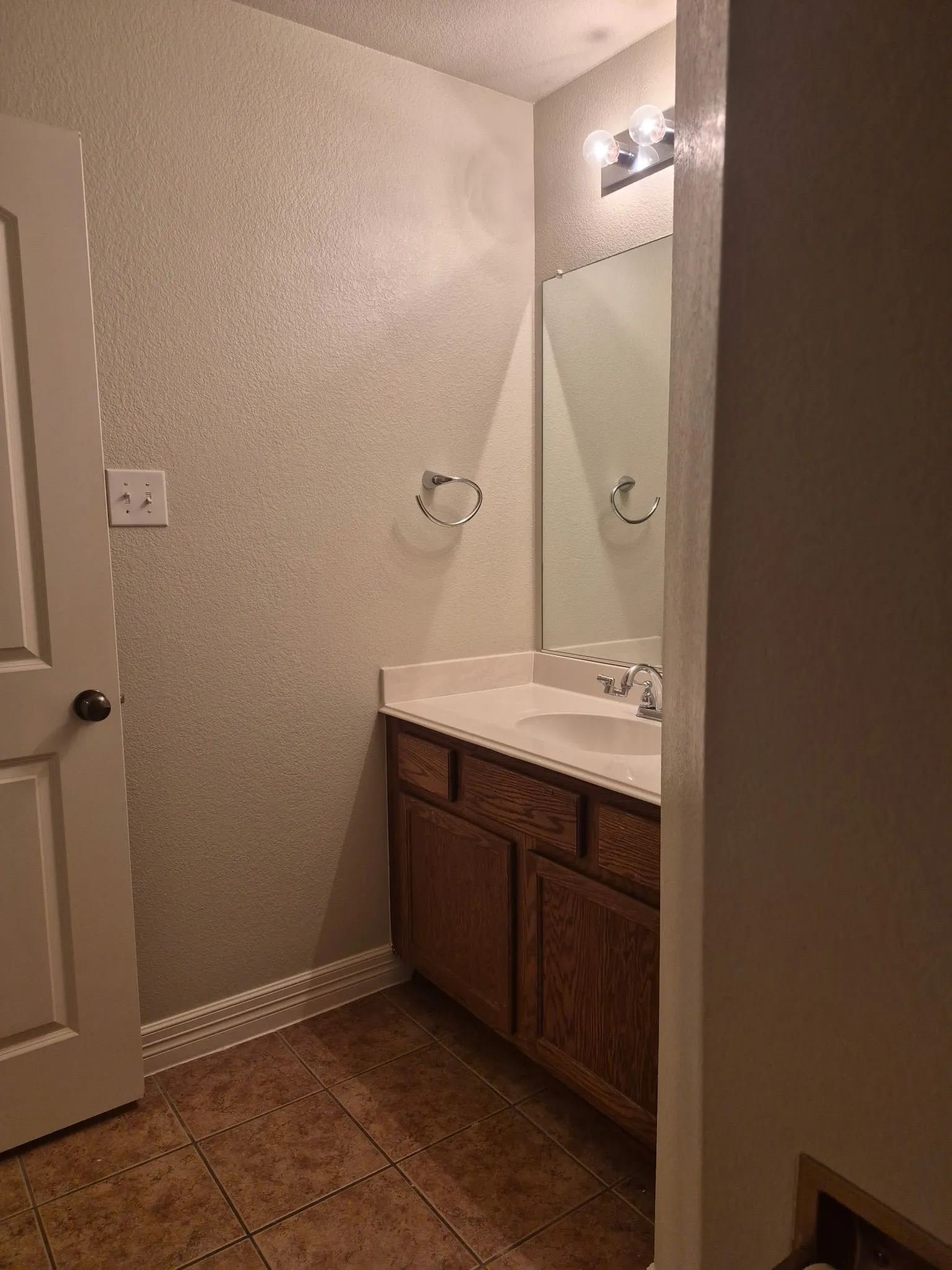 Vanity with a single basin sink, light-toned countertop, wood-finish cabinetry, and a wall-mounted mirror