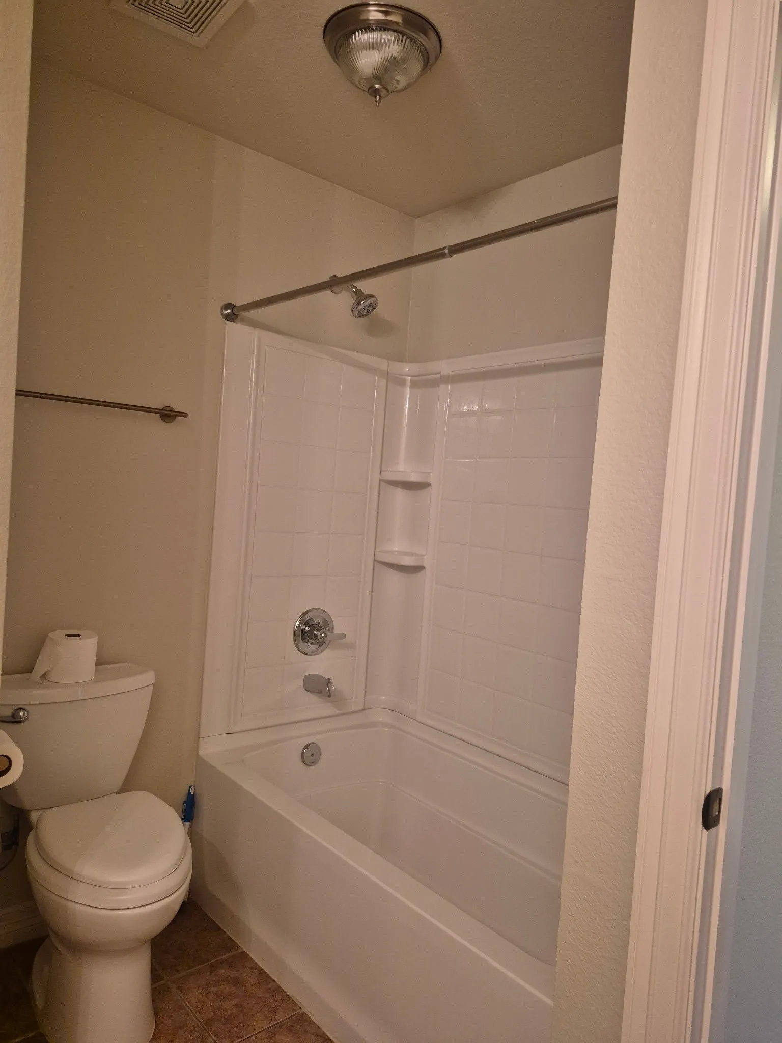 White bathtub and shower combination with chrome fixtures, complemented by a toilet and tile flooring