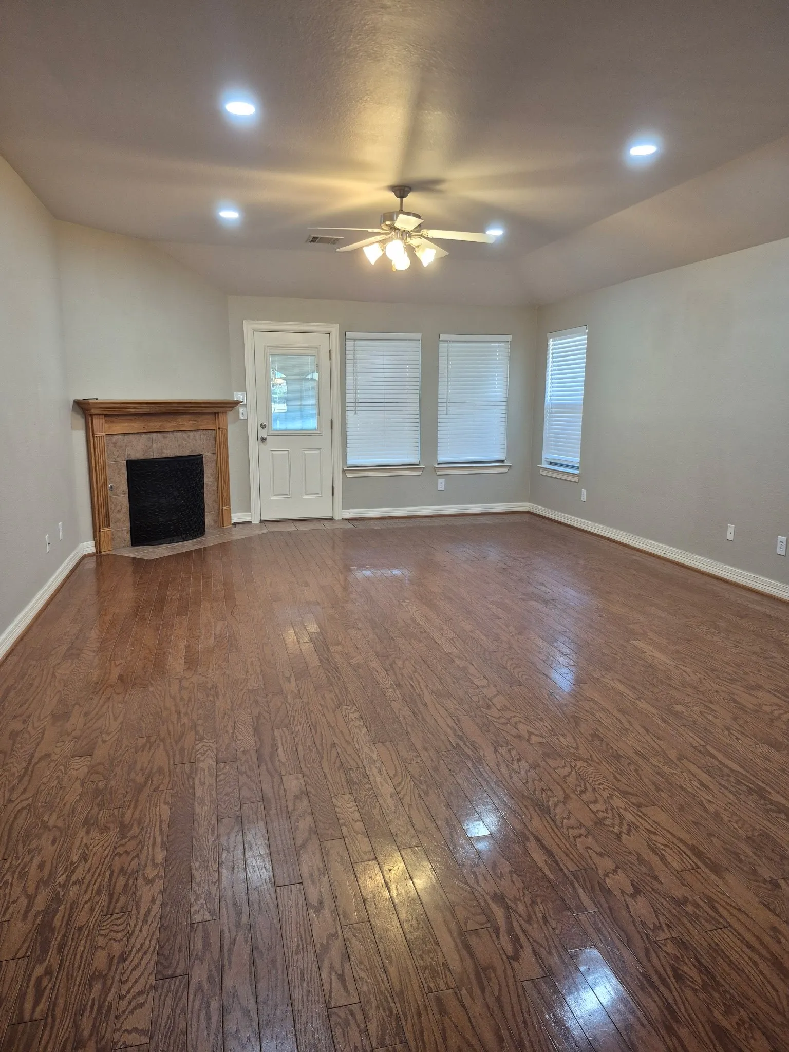 Spacious room with wood-finish flooring, a built-in corner fireplace, and multiple windows with blinds