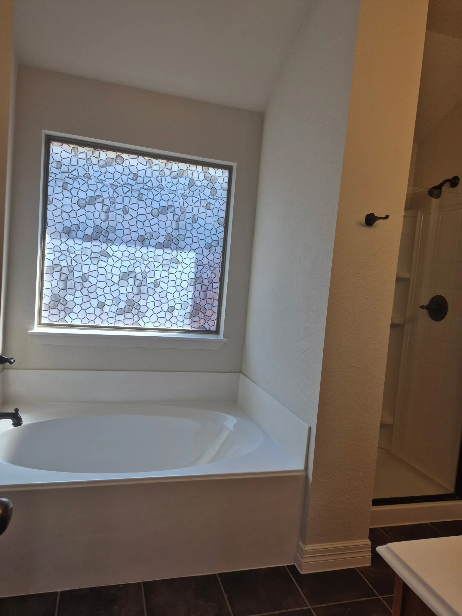 Built-in soaking tub with a patterned privacy window, dark tile flooring, and a shower enclosure