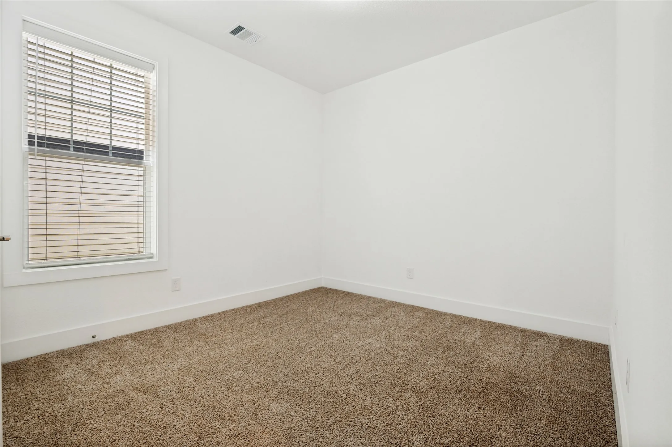 Neutral-toned carpeting, white walls, and a window with blinds