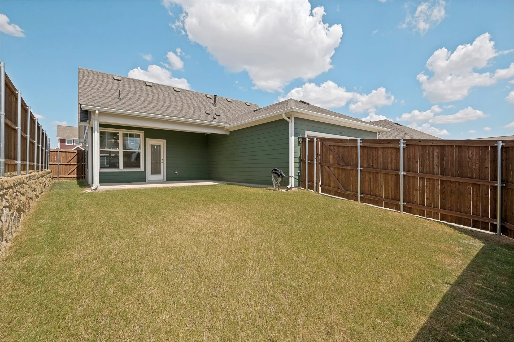 Private backyard with a covered patio, manicured lawn, wood fencing, and a stone retaining wall