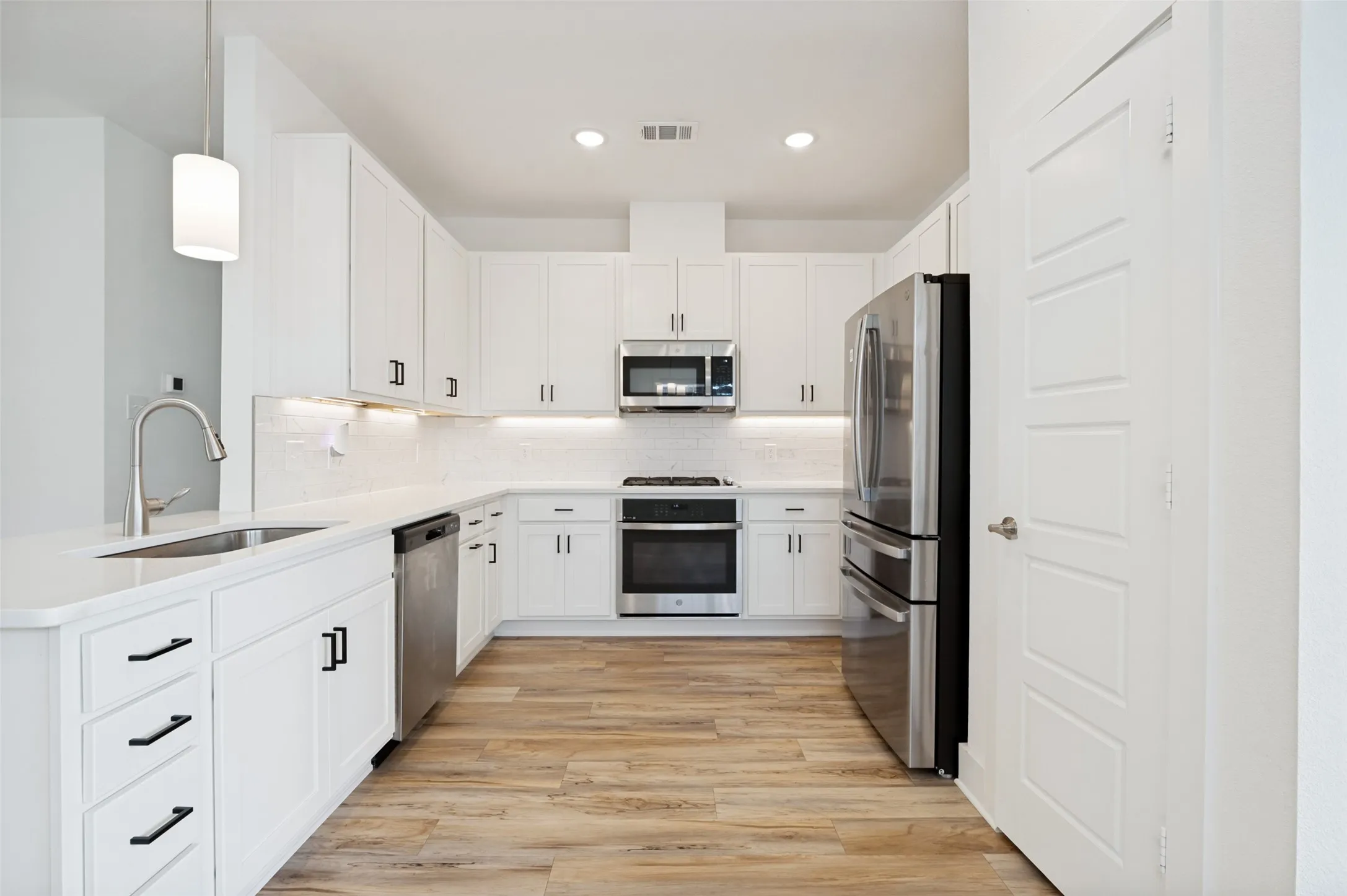 Kitchen featuring stainless steel appliances, white cabinetry with black hardware, wood-finish flooring, a stainless steel sink, and recessed lighting