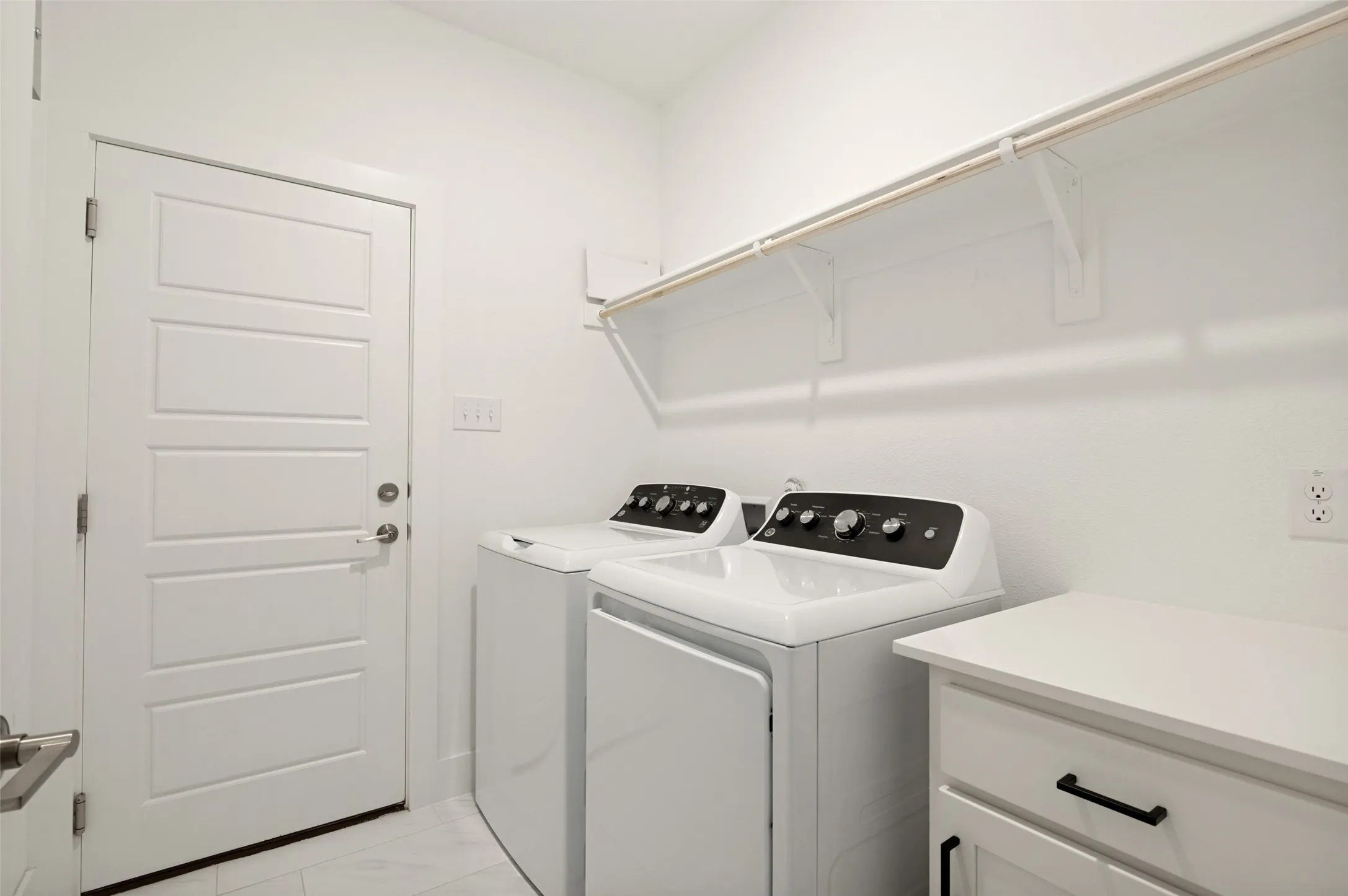 Dedicated laundry area featuring a built-in countertop, white cabinetry with black hardware, and an overhead clothes rod with shelving