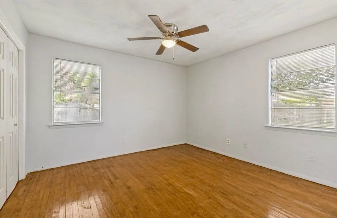 Wood-finish flooring throughout, two windows with blinds, built-in ceiling fan with light fixture, and a paneled closet door