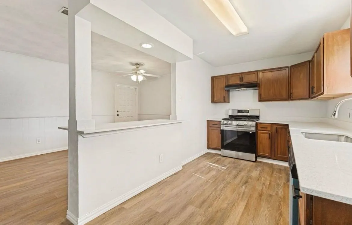Kitchen with wood-finish flooring, stainless steel appliances, wood cabinetry, and solid surface countertops