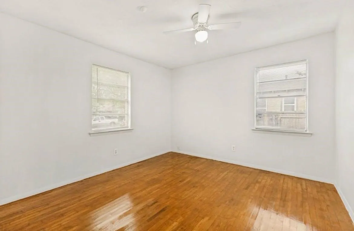 Hardwood flooring, white walls, two windows with blinds, ceiling fan with integrated lighting