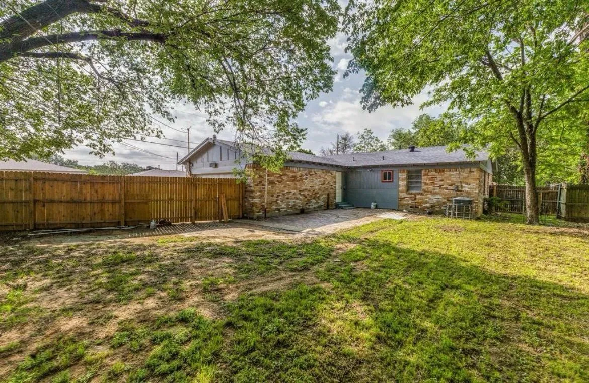 Expansive yard featuring mature trees, a wooden privacy fence, stone exterior, and a shingle roof