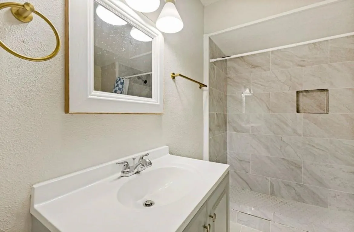 Vanity with integrated sink, chrome faucet, framed mirror, and overhead lighting