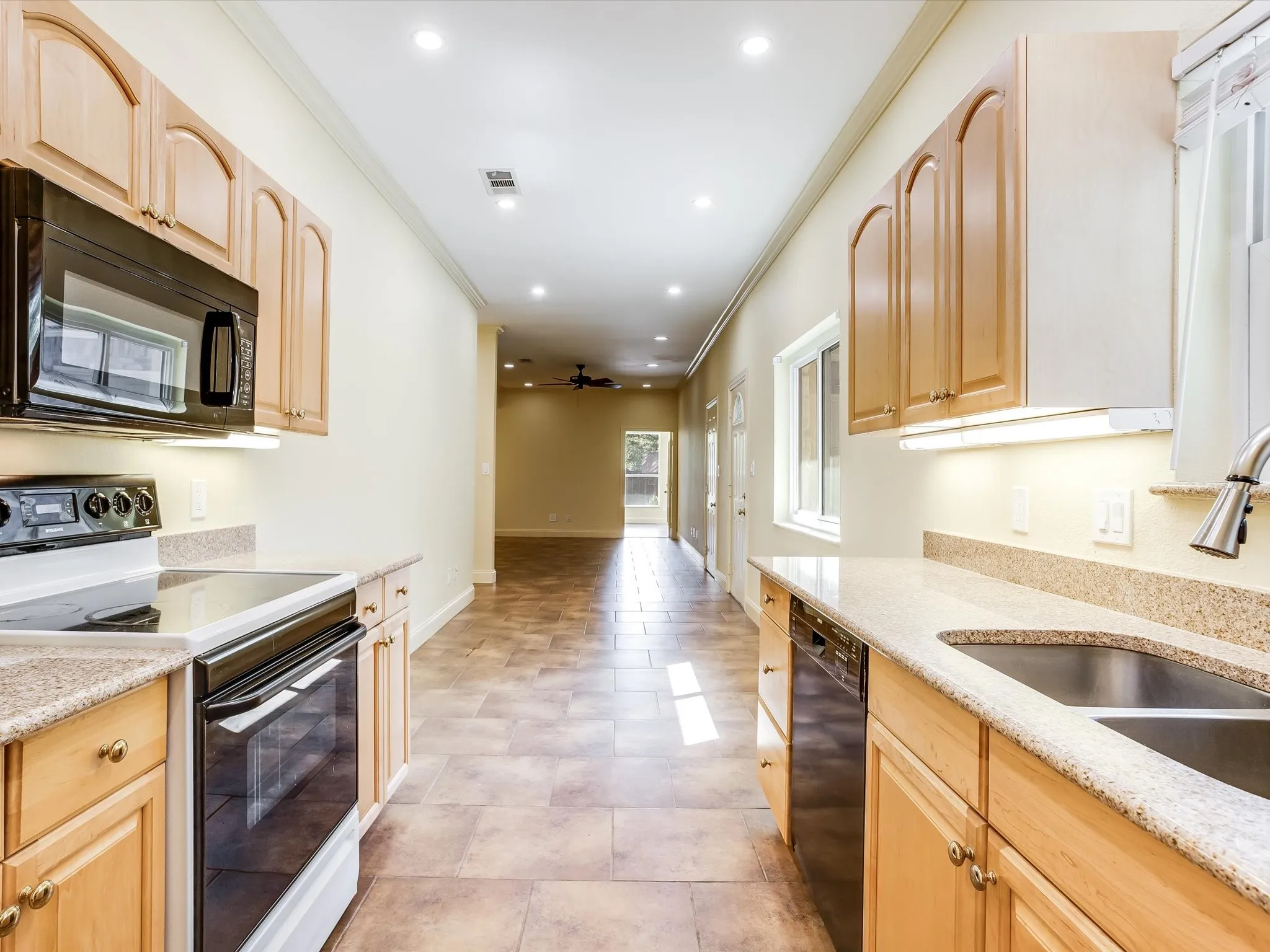Beautiful kitchen in the separate living quarters! Kitchen featuring wood cabinetry, solid surface countertops, stainless steel sink, black range, and black built-in microwave