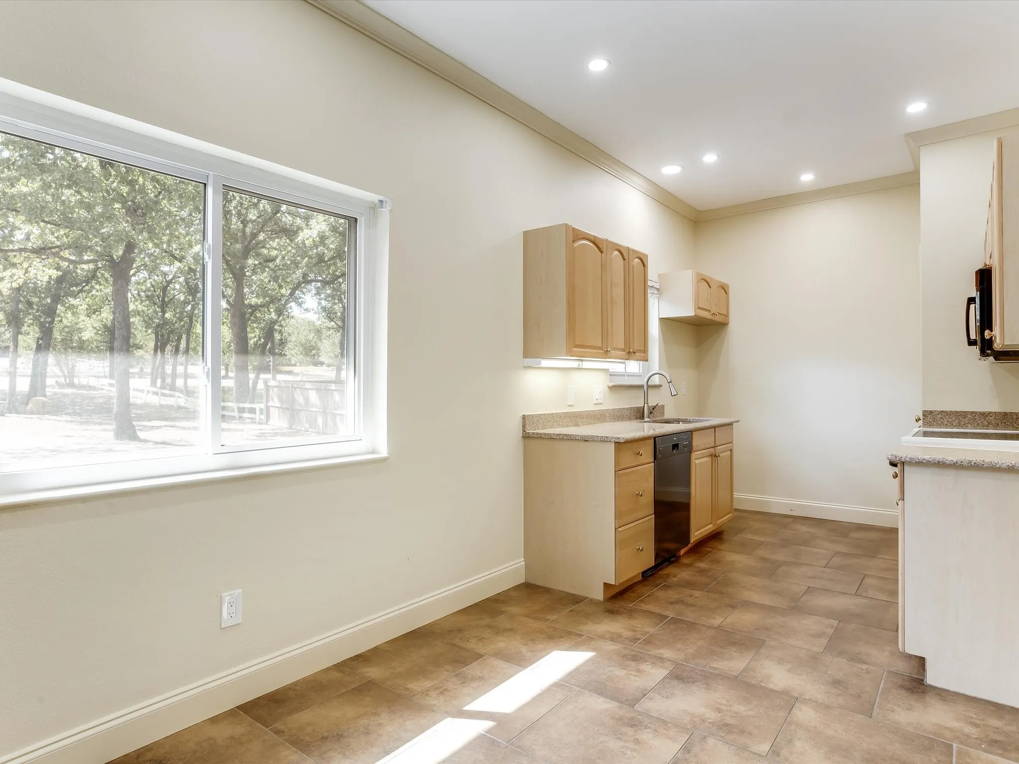 Tons of natural light! Recessed lighting illuminates the kitchen featuring wood-finish cabinetry, light-toned countertops, and a stainless steel dishwasher