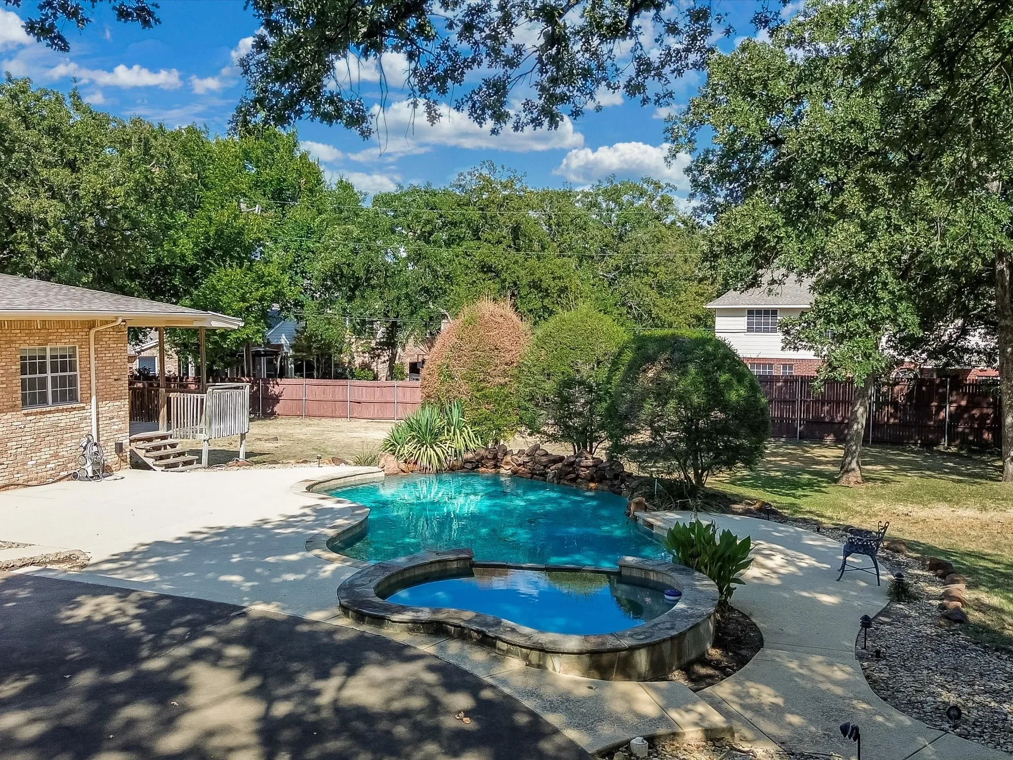 Swimming pool with integrated spa, surrounding concrete patio, and mature trees