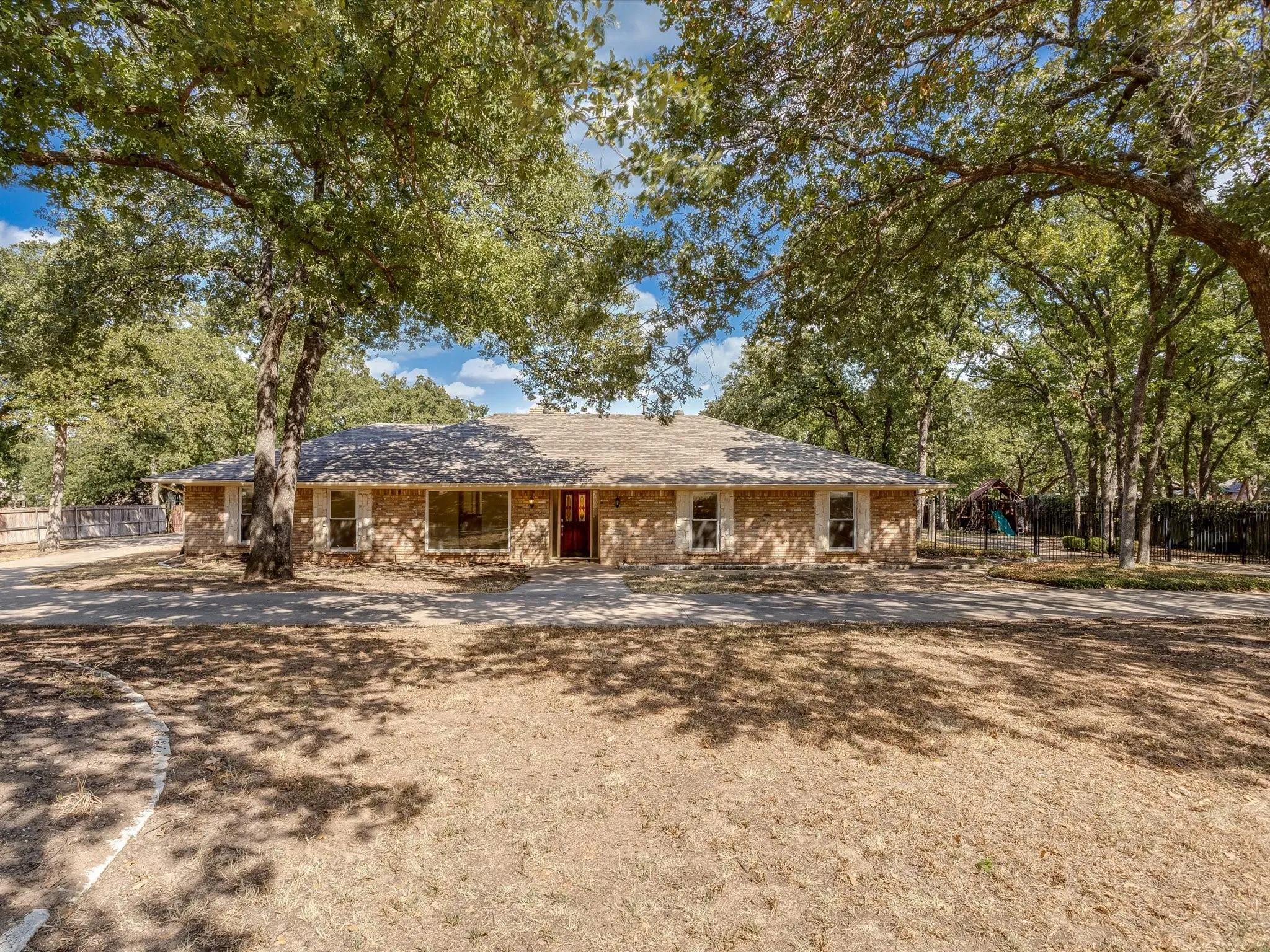 Brick exterior residence with a shingle roof, mature trees, and a circular driveway