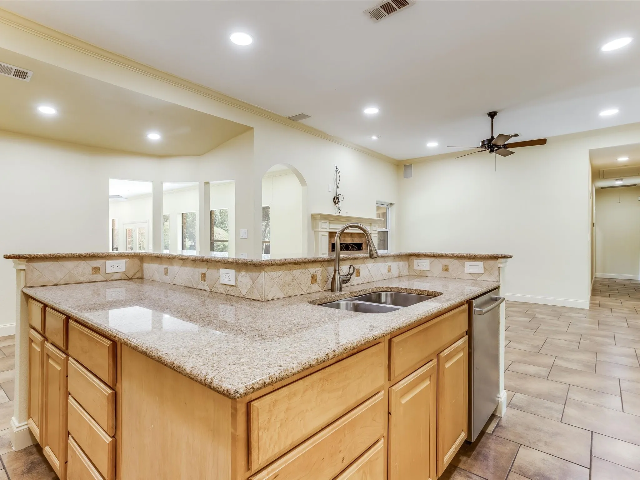 Kitchen island with stone-finish countertops, stainless steel double-basin sink, and light wood cabinetry