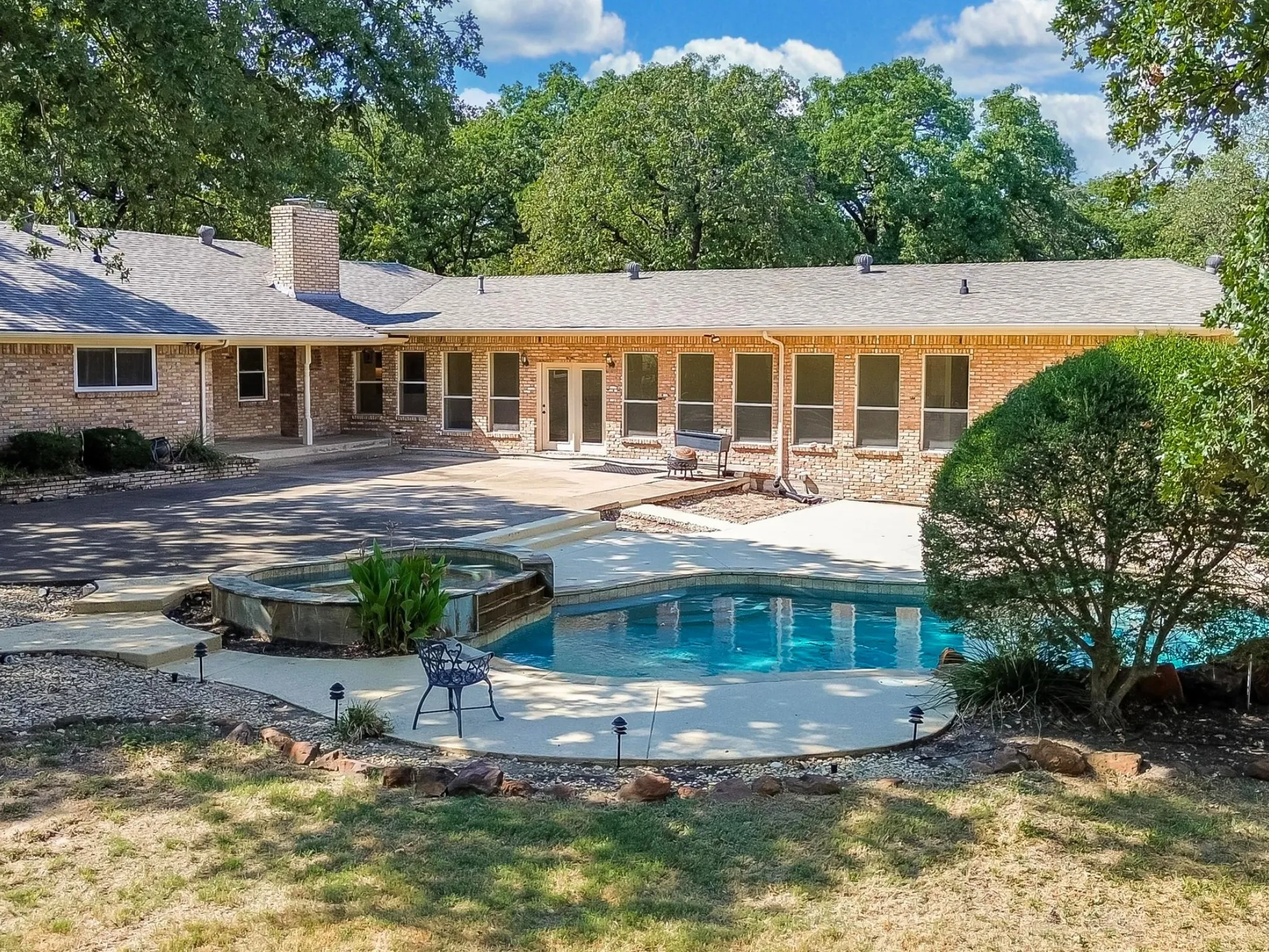 Brick exterior residence featuring a swimming pool, integrated spa, and concrete patio