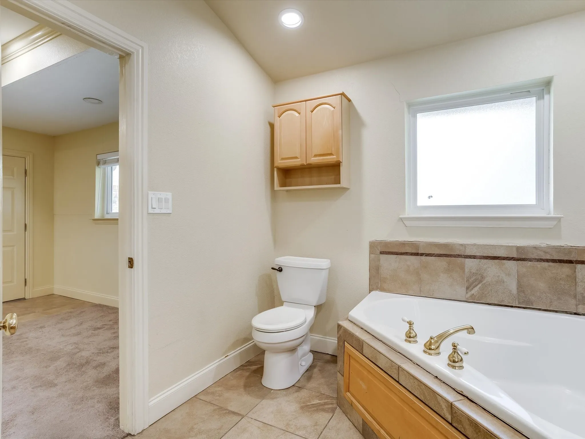 Primary Bathroom. Bathroom featuring tile flooring, built-in soaking tub with brass fixtures, wood-finish cabinetry, and a window
