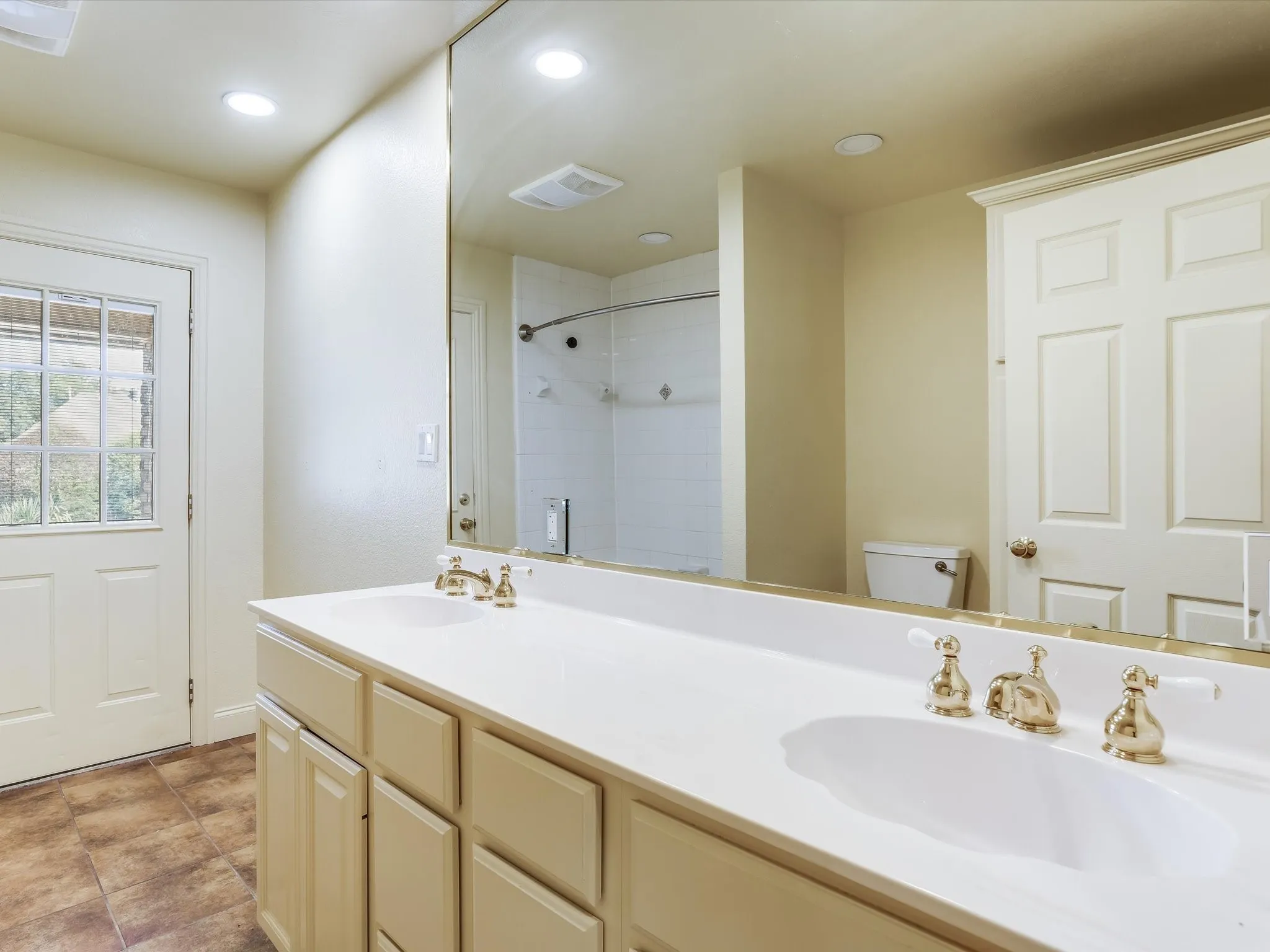Guest bathroom. Dual vanity with integrated sinks, brass-finish faucets, and an expansive mirror