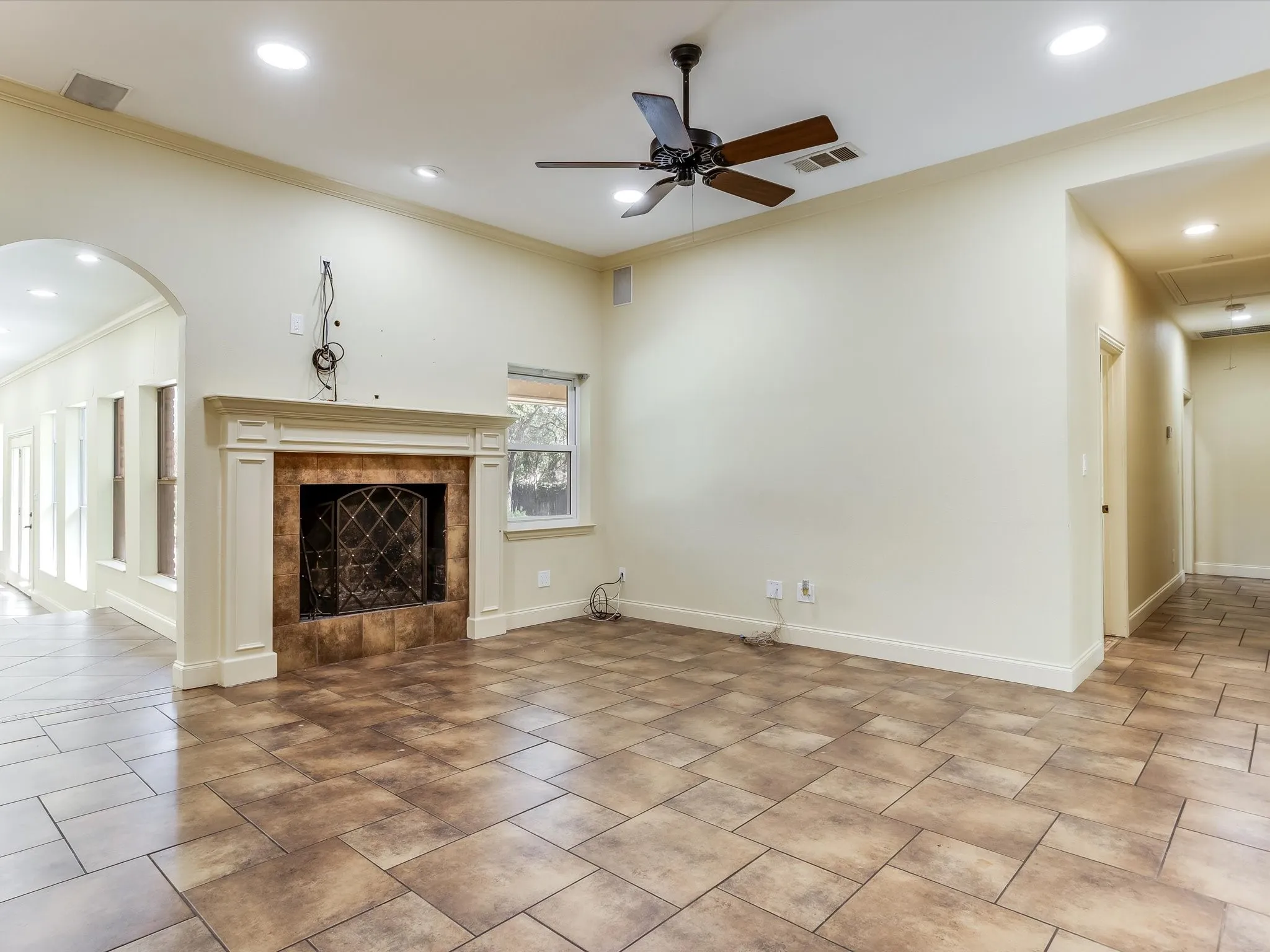 Tiled flooring, fireplace with decorative mantel, recessed lighting, ceiling fan, and arched doorway