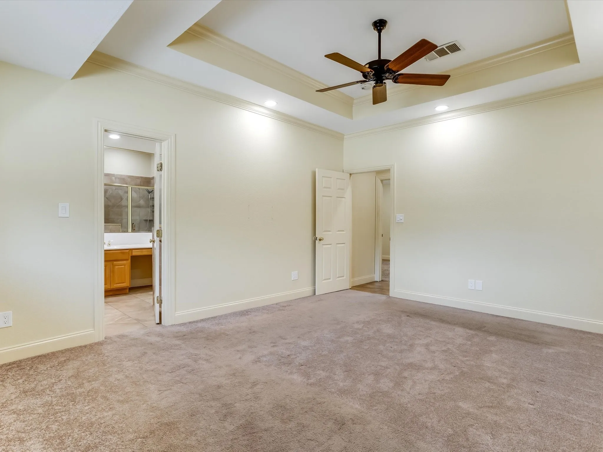 Primary Bedroom. Recessed lighting, ceiling fan, tray ceiling, carpet flooring, and crown molding