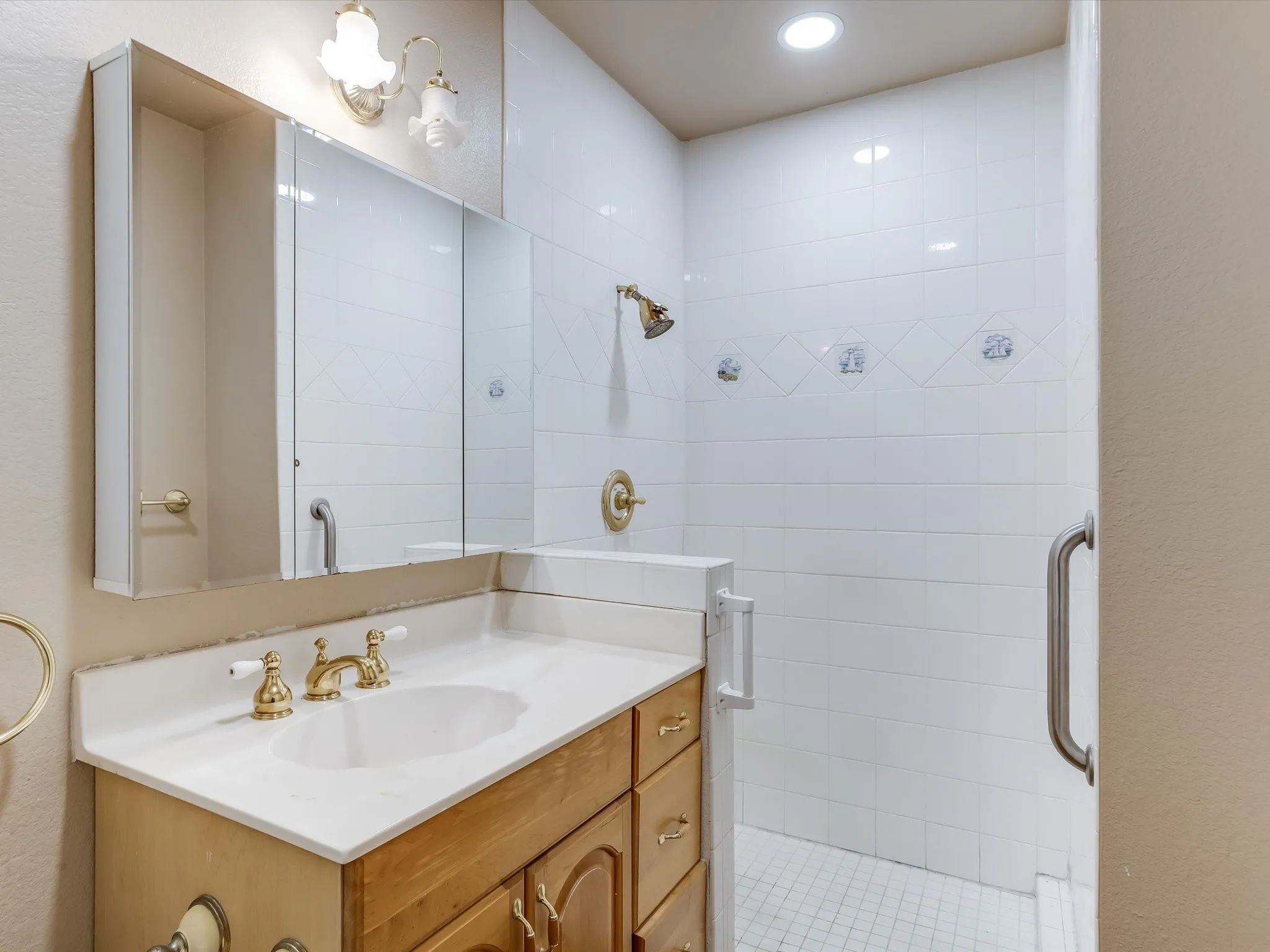 Bathroom in the separate living quarters. White tiled shower with decorative accent line and gold-finish fixtures