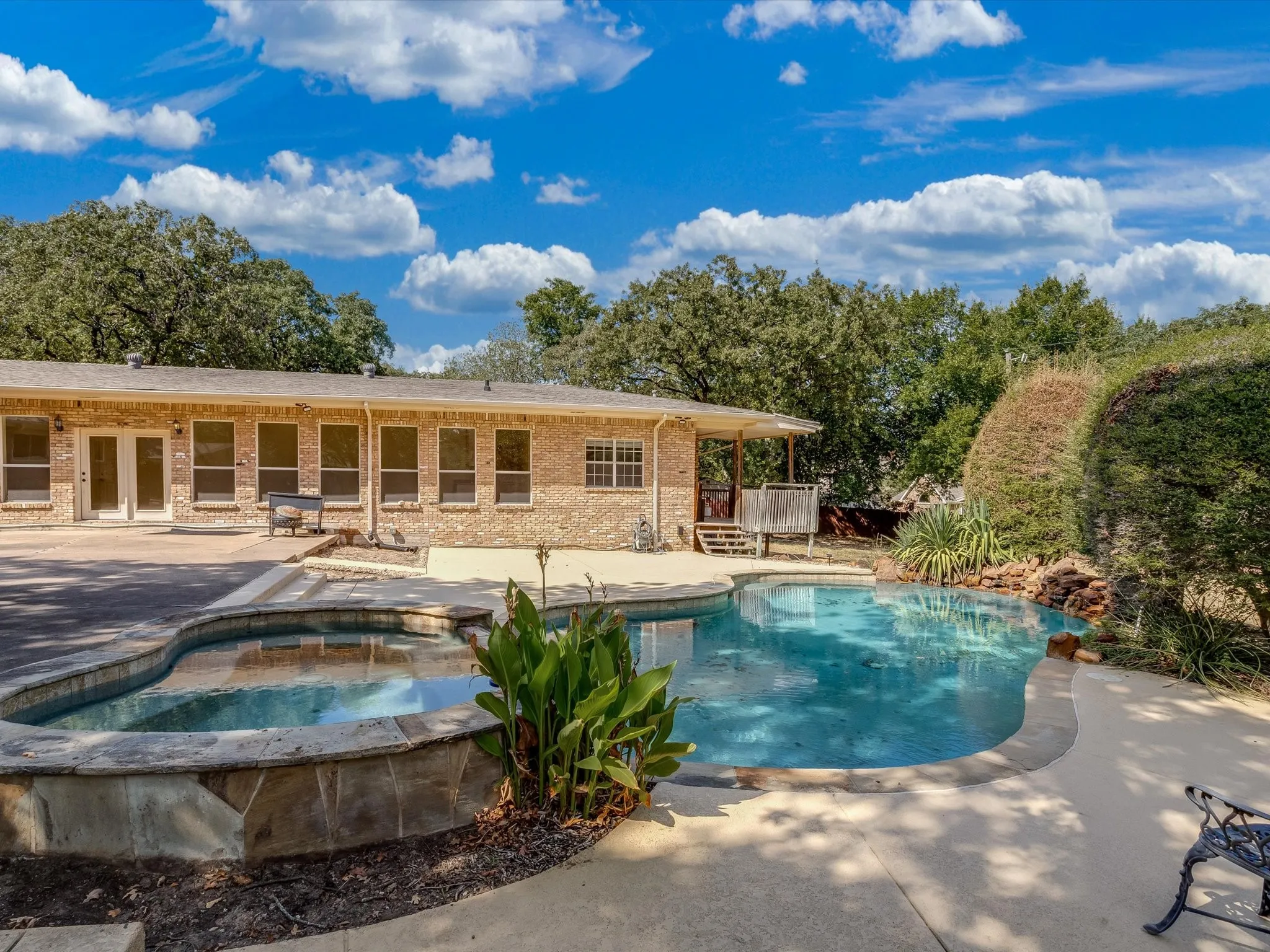 Exterior featuring a brick facade, multiple large windows, a swimming pool, and a spa with stone surround
