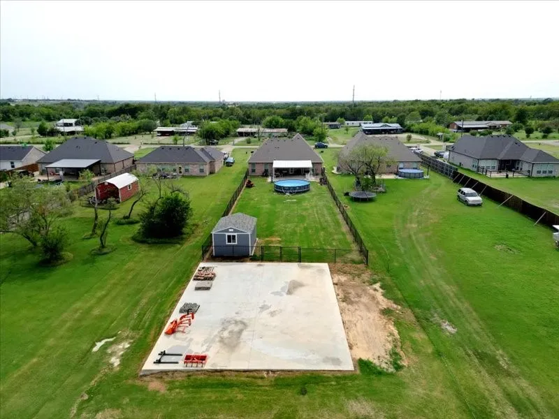 Large concrete pad, detached storage shed, expansive green lawn, black metal fencing, and mature trees
