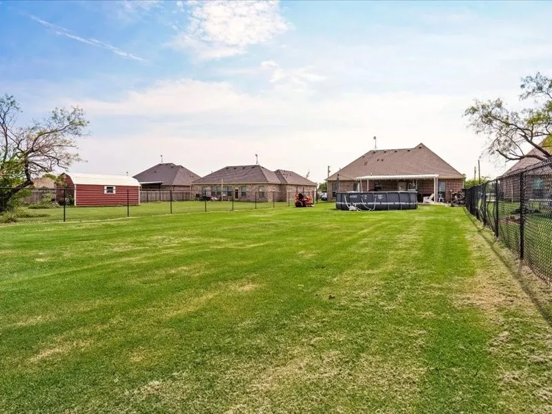 Expansive grassy yard with a red storage shed and chain-link fencing