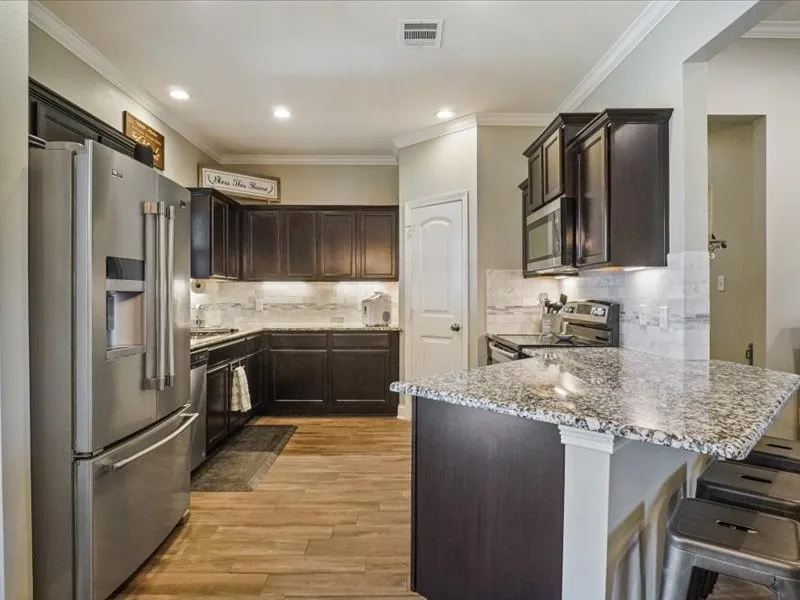 Kitchen featuring dark wood-finish cabinetry, granite countertops, stainless steel appliances, wood-finish flooring, and a tile backsplash