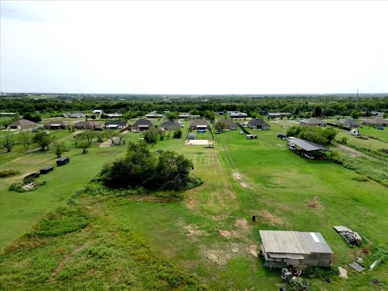 Expansive green space featuring scattered mature trees and a distant residential area