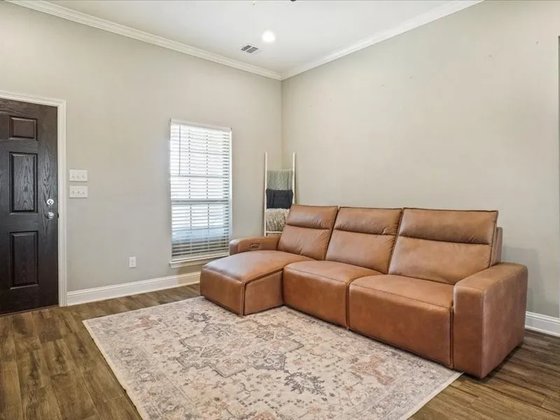 Wood-finish flooring, white crown molding, and a dark paneled door with brushed nickel hardware