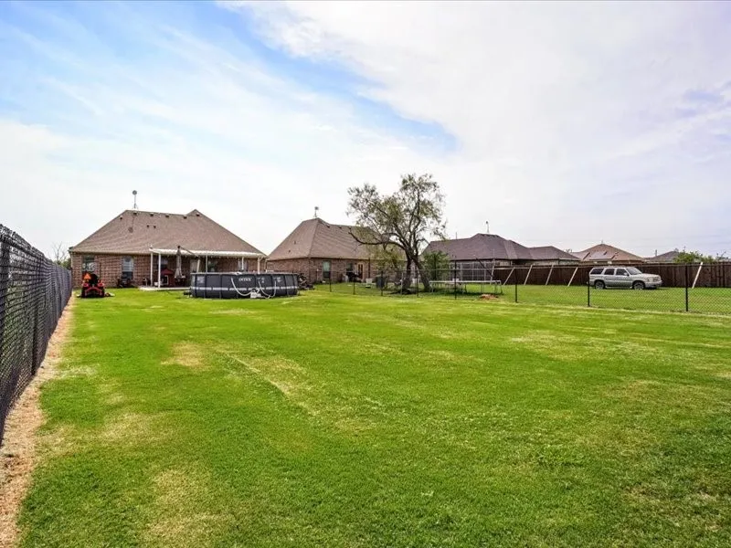 Expansive rear yard featuring a chain-link fence, a covered patio, and mature trees